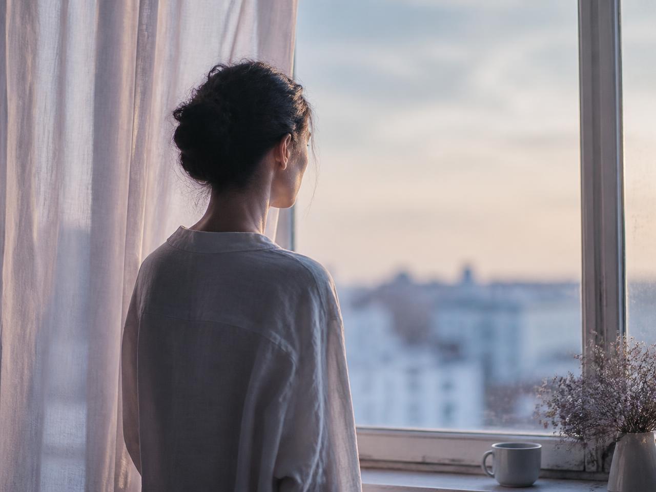 Pessoa em pé junto à janela, em um momento de pausa e reflexão